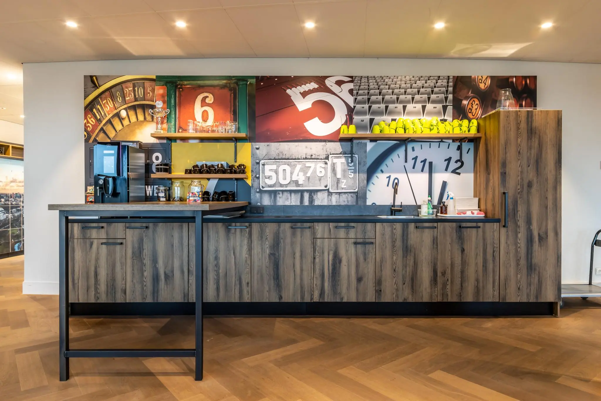 Moderne koffie- en pantryhoek met houtlook kastjes en kleurrijke fotocollage op de achterwand aan de Fascinatio Boulevard.